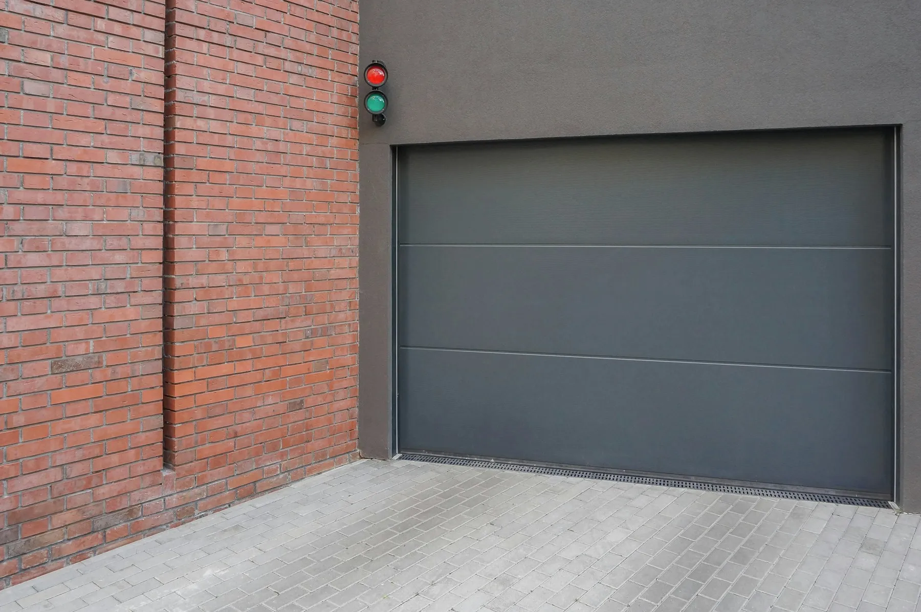 A dark gray flush steel garage door beside a brick wall
